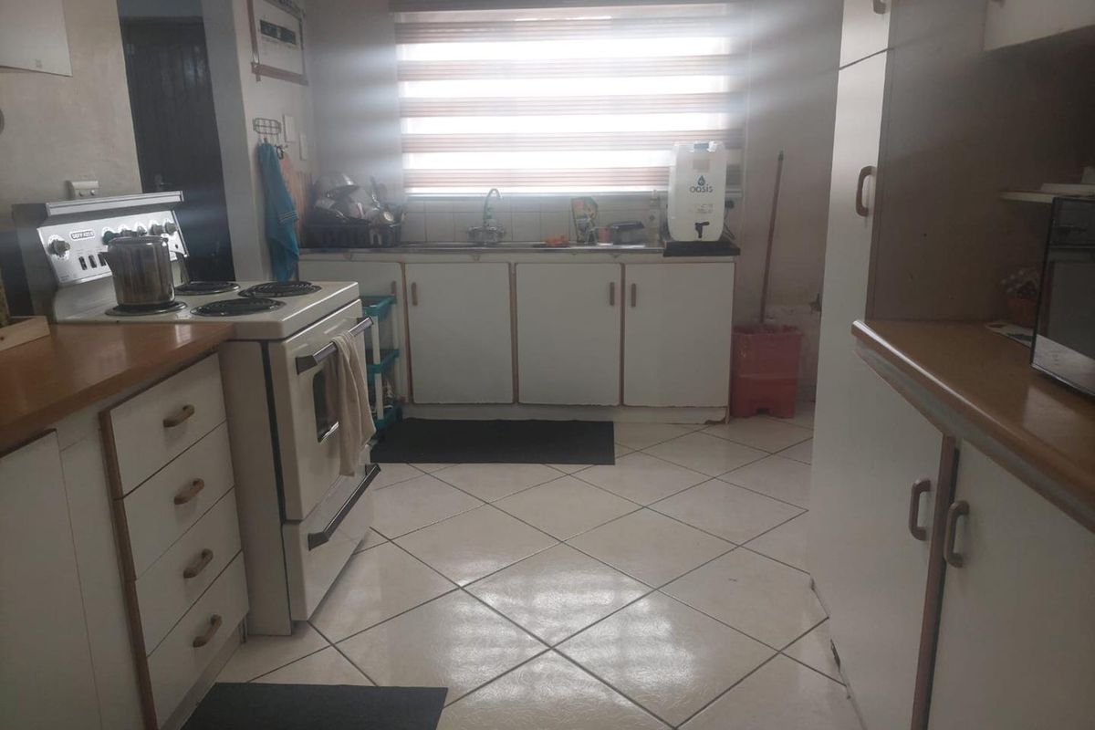 A functional kitchen featuring white cabinetry, laminate countertops, a freestanding stove, and tiled flooring, offering a practical layout with potential for modern updates.