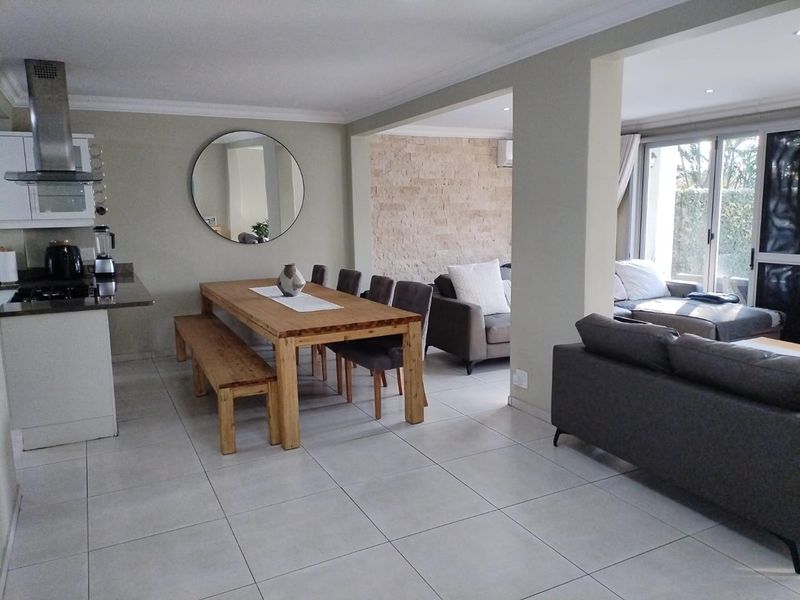 Spacious open-plan living and dining area featuring tiled floors, a stone accent wall, and seamless flow to the outdoor patio through sliding glass doors.