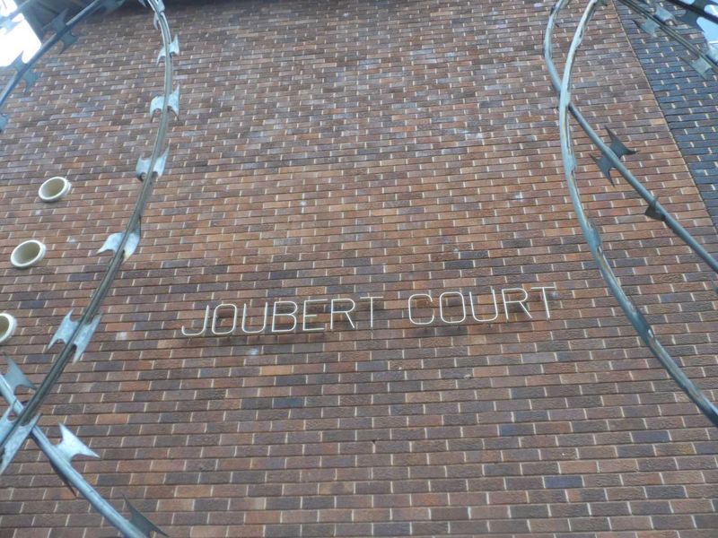 Exterior view of the Joubert Court building facade featuring brickwork and security razor wire fencing.