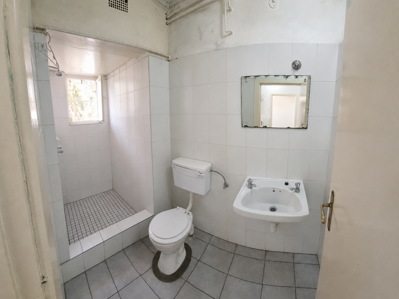 A functional bathroom featuring a walk-in shower, wall-mounted basin, and toilet, with tiled finishes throughout. The space is ready for modernization.