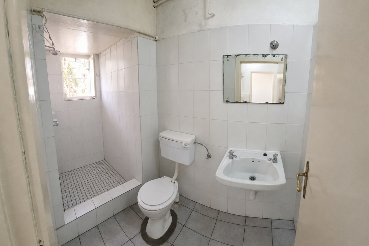 A functional bathroom featuring a walk-in shower, wall-mounted basin, and toilet, with tiled finishes throughout. The space is ready for modernization.