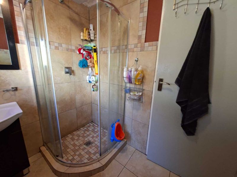 A functional bathroom featuring a corner shower enclosure with tiled walls and flooring, complemented by a wall-mounted basin.