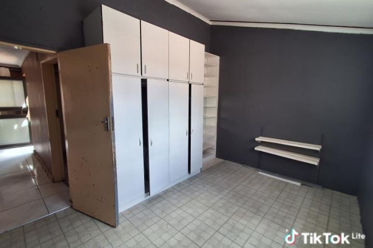 A bedroom featuring built-in white cabinetry, dark painted walls, and tiled flooring, offering functional storage space.
