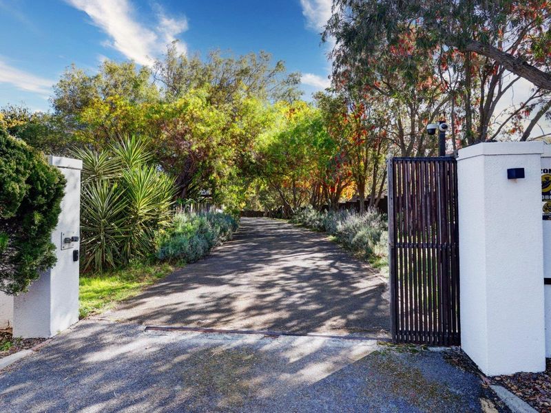 A private entrance featuring a secure gated driveway flanked by established trees and perimeter walls, providing access to the property.
