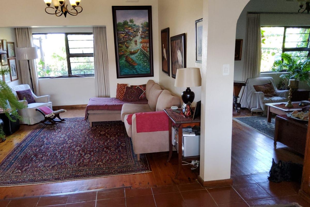 A spacious living area featuring hardwood and tiled flooring, connected by an architectural archway to an adjacent room with large windows.