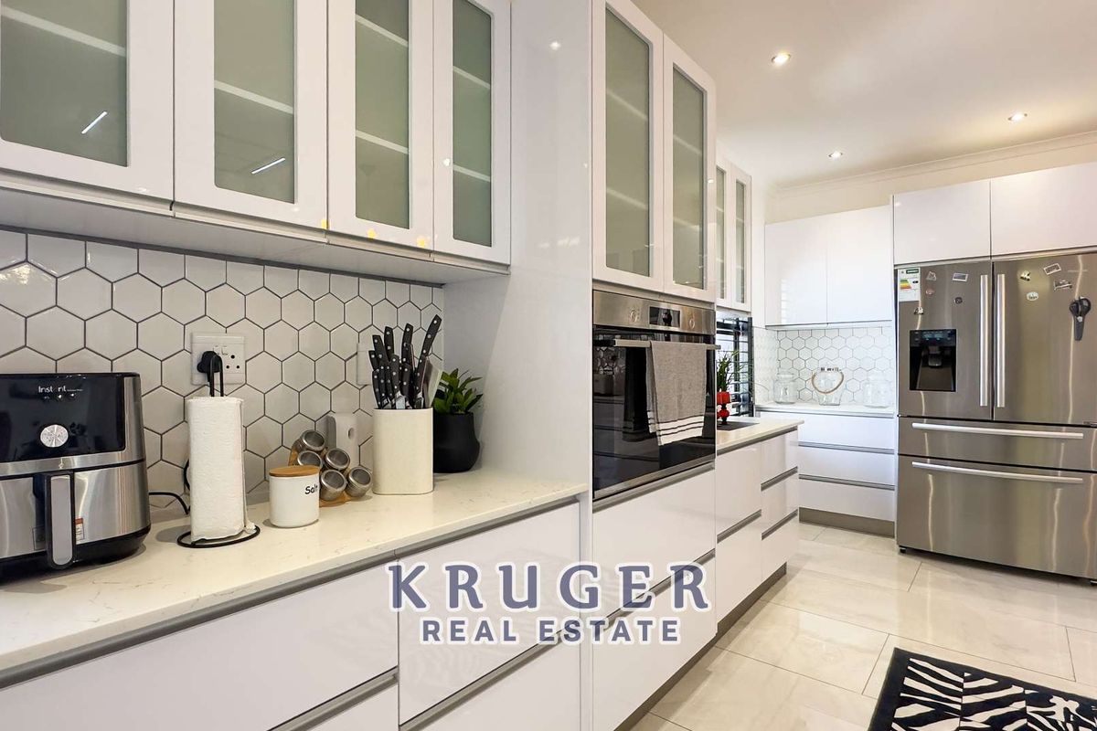 Modern kitchen featuring high-gloss white cabinetry, stone countertops, a stylish hexagonal tile backsplash, and integrated stainless steel oven.