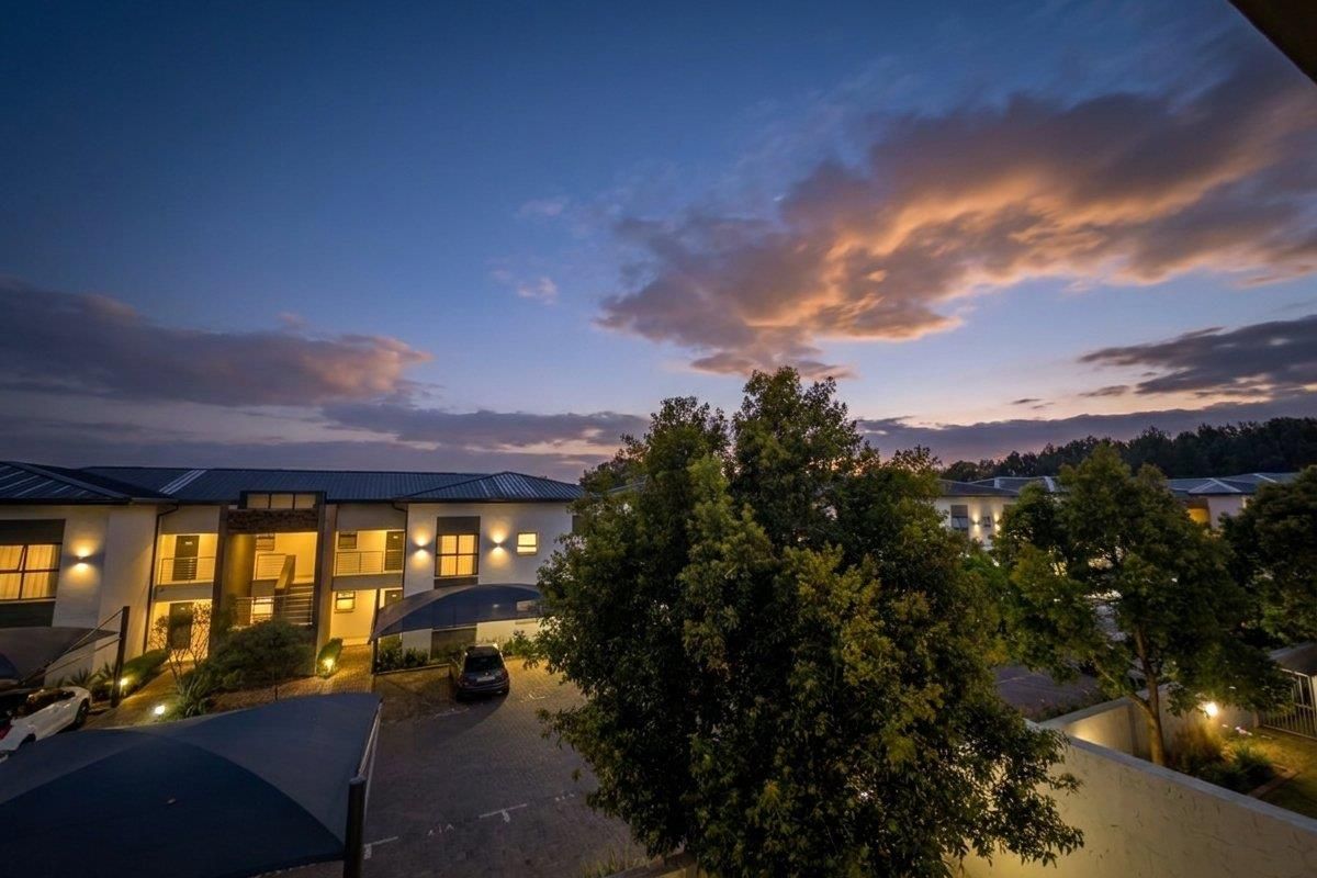 An elevated evening view of the apartment complex exterior, featuring paved parking areas, carport structures, and well-maintained building facades with ambient lighting.