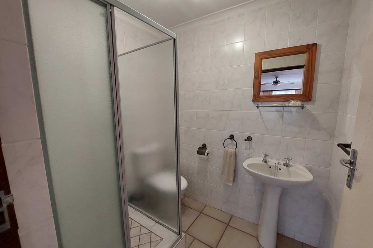 A functional bathroom featuring a shower enclosure, pedestal basin, and toilet with neutral wall and floor tiling.