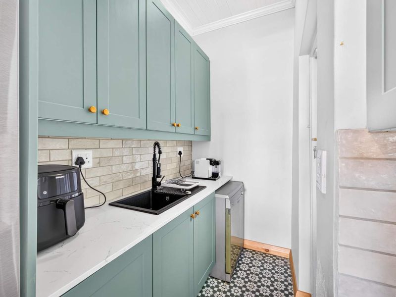 A modern, well-appointed scullery featuring sage green cabinetry, stone countertops, a sleek black sink, and stylish patterned floor tiles.