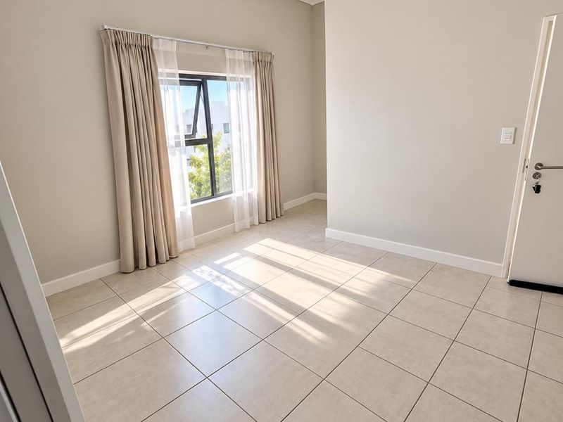 A bright, empty bedroom featuring neutral tiled flooring, clean wall finishes, and a top-hung window with installed curtain tracks.