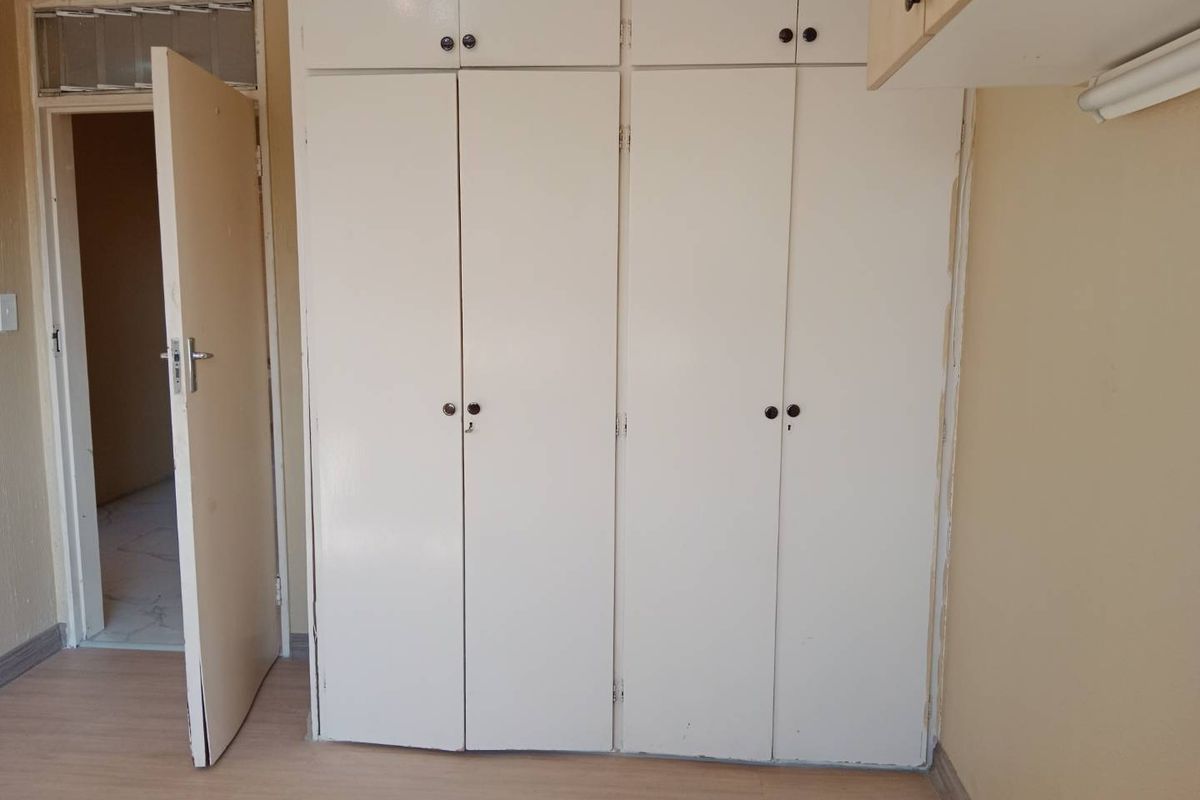 A bedroom featuring built-in cupboards with overhead storage and laminate flooring, presenting a blank canvas for potential interior updates.