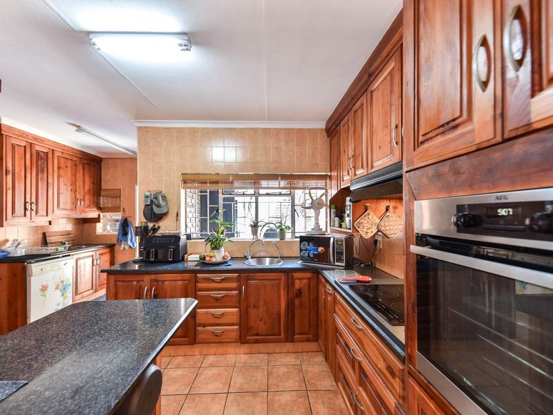A functional kitchen featuring extensive wooden cabinetry, granite countertops, built-in oven, electric hob, and tiled finishes throughout.