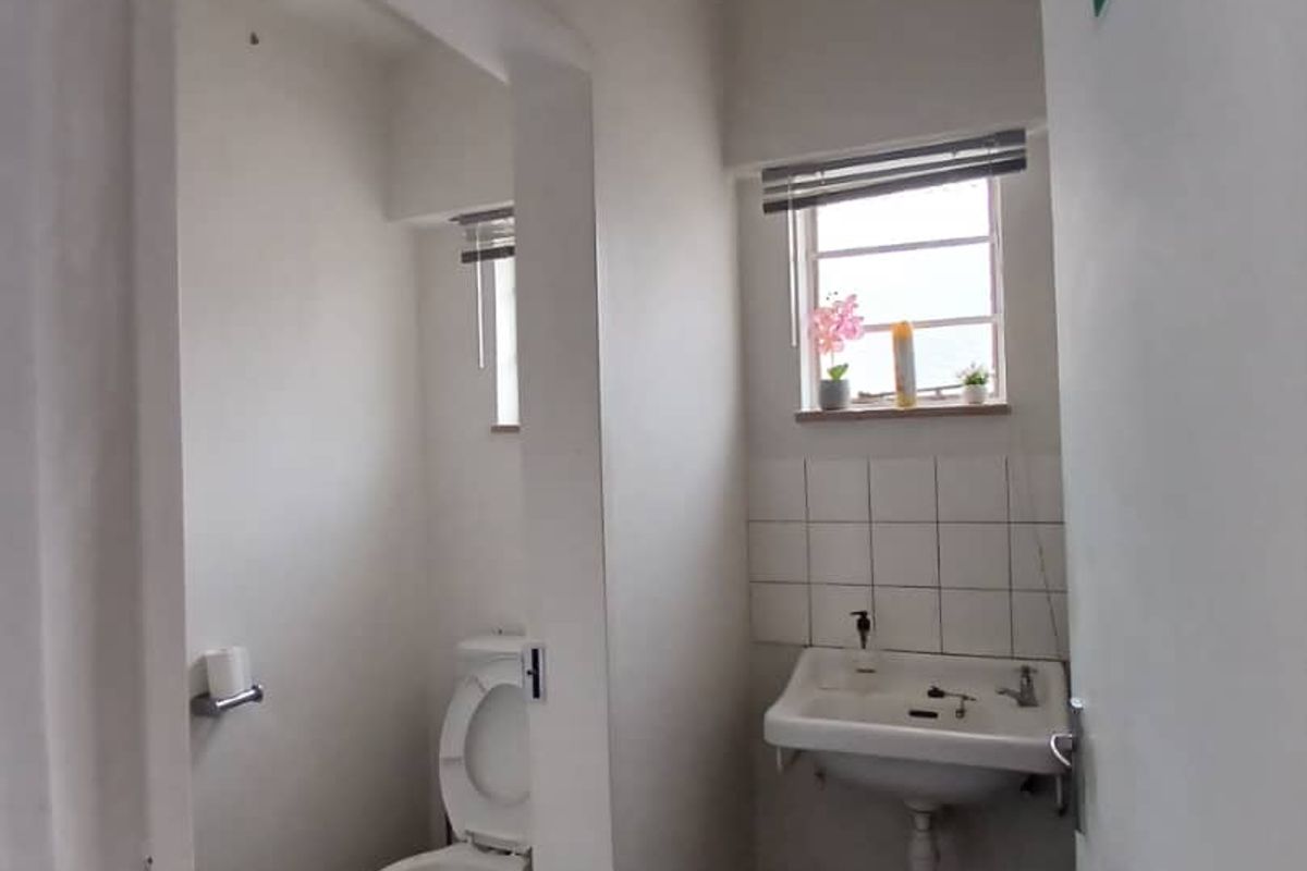 A functional, compact commercial restroom featuring a wall-mounted basin with tiled splashback and a separate toilet cubicle area.