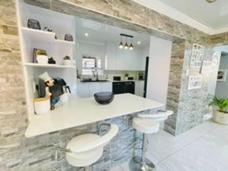 Modern kitchen featuring a stone-clad breakfast bar, built-in shelving, and sleek white cabinetry, creating a bright and functional culinary space.
