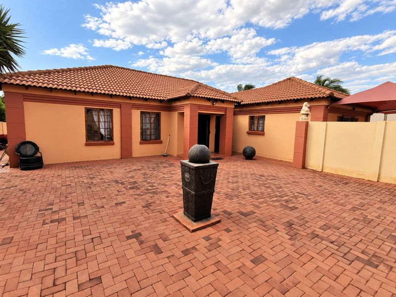 Front exterior view of a single-story house featuring a paved courtyard, terracotta tiled roof, and secure boundary walling.