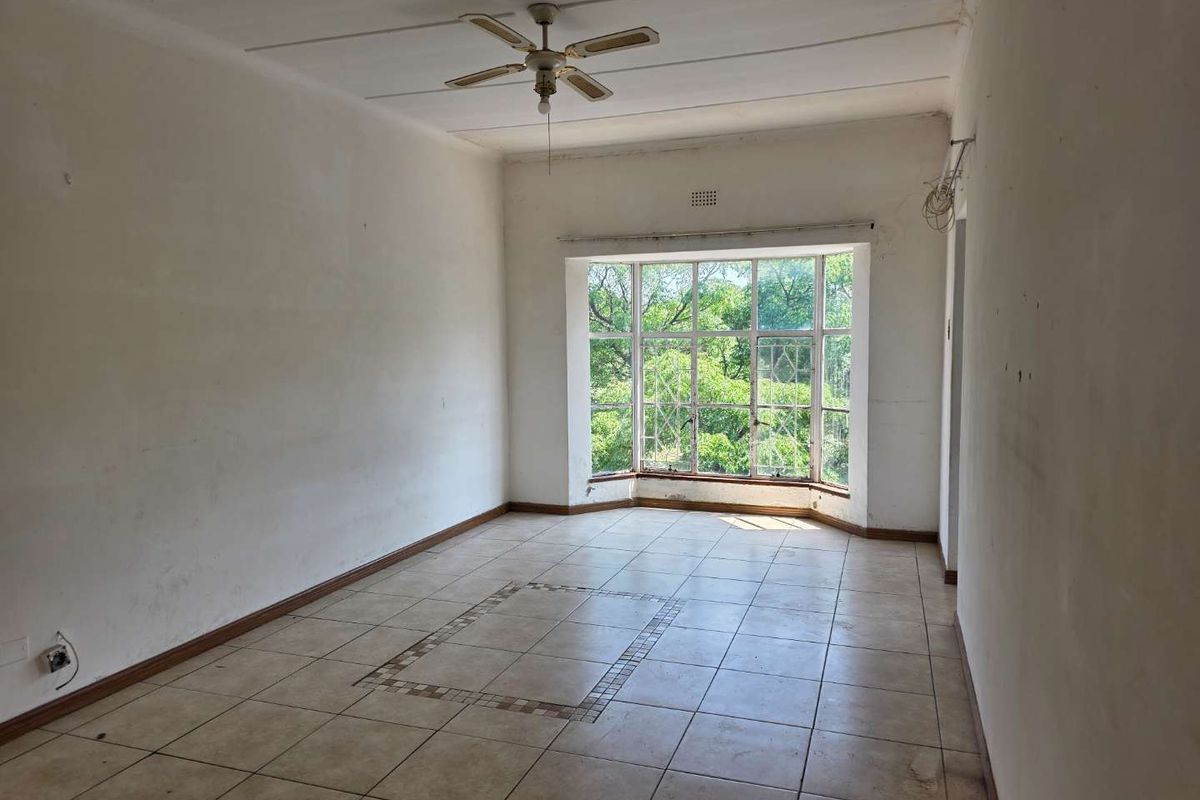 A vacant living room featuring large bay windows, tiled flooring with a decorative inlay, and a ceiling fan.