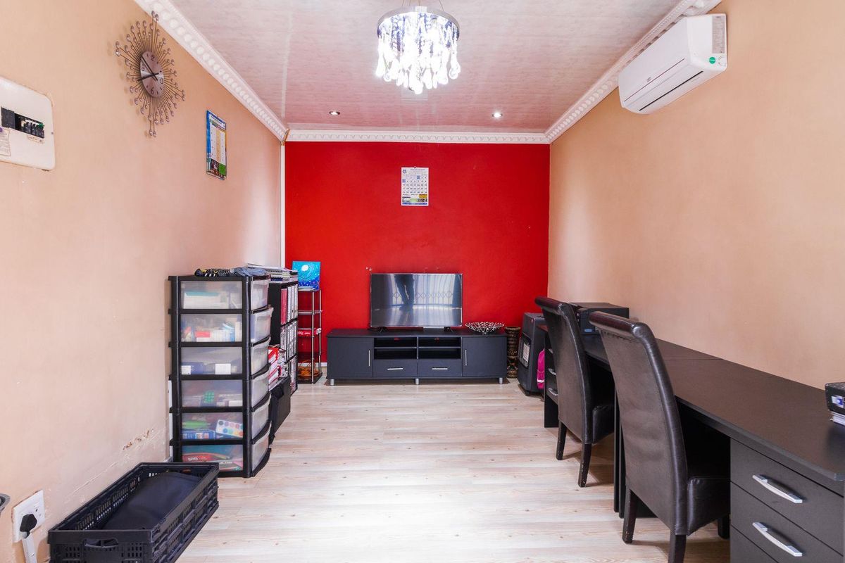 A functional living room or office space featuring light wood-look flooring, a bold red accent wall, crown molding, and a wall-mounted air conditioning unit.