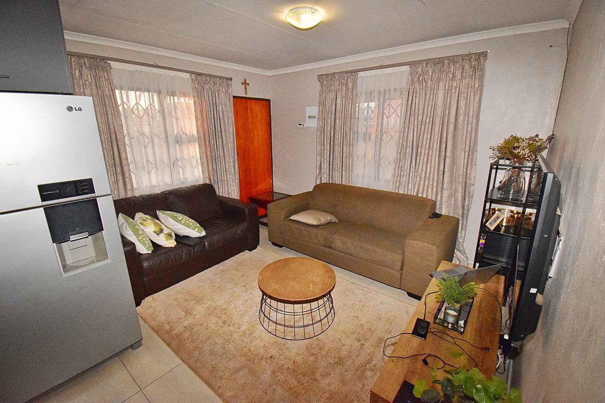 A living room featuring tiled flooring, dual windows with curtains, and a central ceiling light fixture.