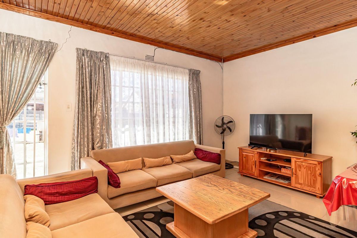 A living room featuring tiled flooring and a timber tongue and groove ceiling, with access to the exterior via a sliding glass door.