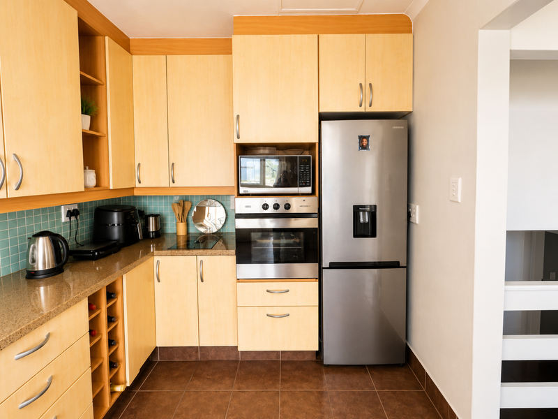 A functional kitchen featuring light wood cabinetry, granite countertops, a tiled backsplash, and integrated stainless steel appliances including an oven and microwave.