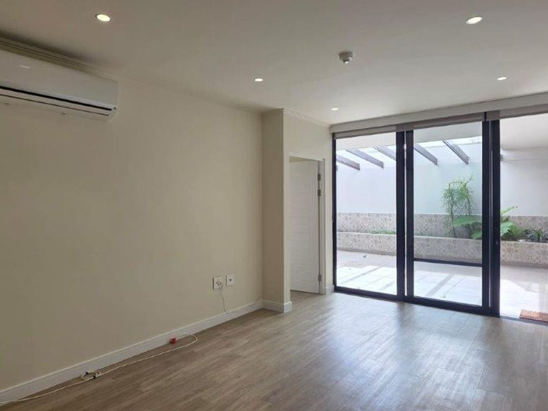 A bright, empty living room featuring modern laminate flooring, recessed lighting, a wall-mounted air conditioner, and large sliding doors leading to a private patio.