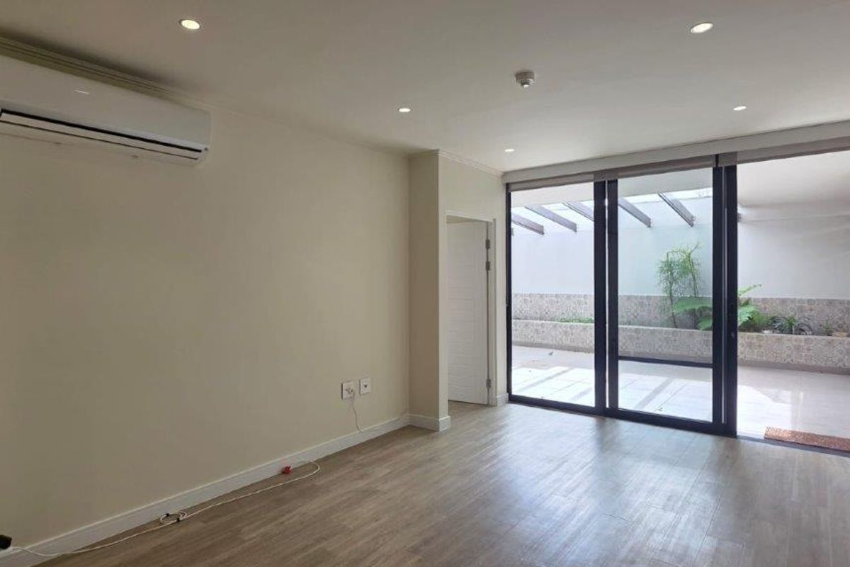 A bright, empty living room featuring modern laminate flooring, recessed lighting, a wall-mounted air conditioner, and large sliding doors leading to a private patio.