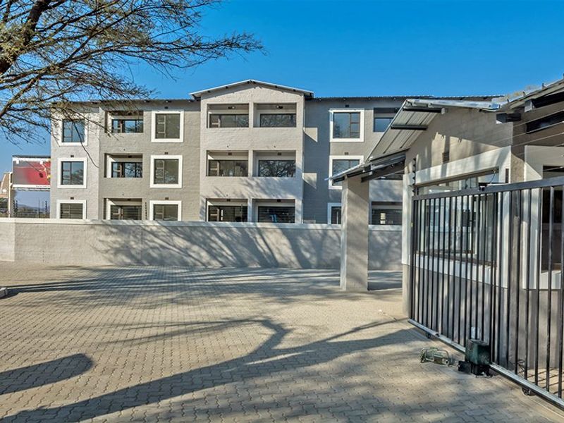 A view of the apartment complex entrance featuring a paved driveway, secure gated access, and perimeter walling with electric fencing.