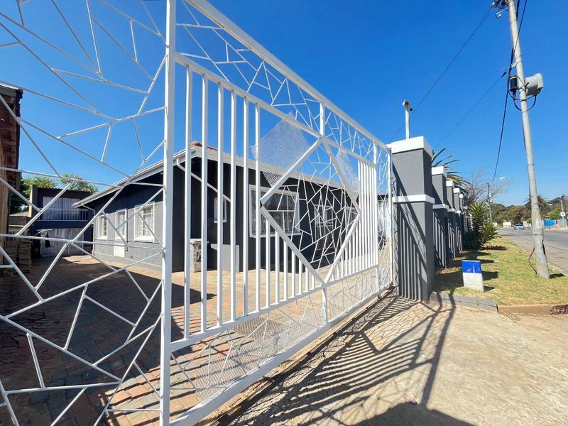 Front view of the property featuring a modern decorative white metal gate, paved driveway, and secure masonry boundary wall.