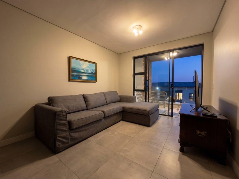 A well-maintained living room featuring neutral tiled flooring and a large sliding glass door that provides access to an outdoor balcony area.
