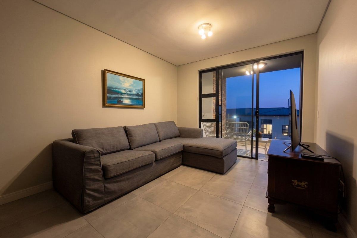 A well-maintained living room featuring neutral tiled flooring and a large sliding glass door that provides access to an outdoor balcony area.