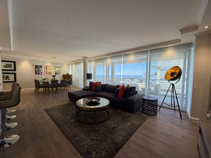 Spacious open-plan living and dining area featuring modern laminate flooring, recessed lighting, and large sliding glass doors leading to a balcony with ocean views.