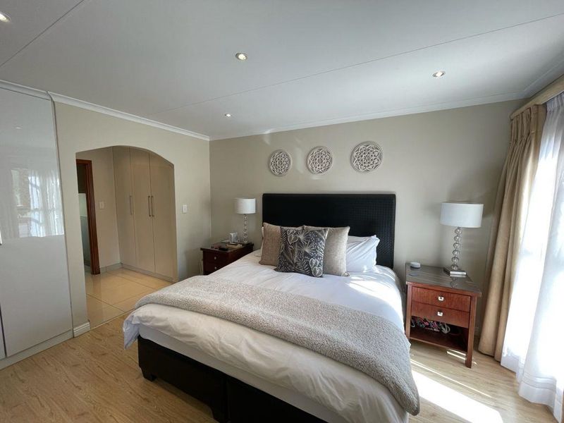 A well-maintained bedroom featuring laminate flooring, recessed downlighting, and built-in cupboards with a neutral color palette.