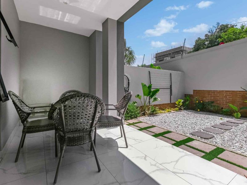 A modern covered patio featuring sleek tiled flooring, leading out to a low-maintenance gravel garden with stepping stones and a secure boundary wall.