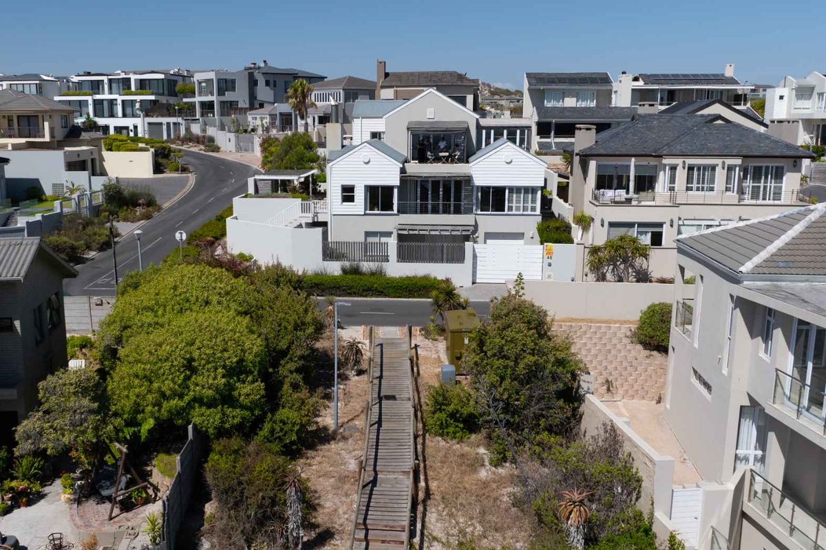 Aerial view of a multi-level residential property featuring a wooden walkway, landscaped garden, and modern architectural design in a coastal neighborhood setting.