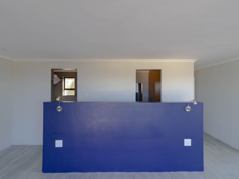 An empty bedroom featuring a central blue partition wall with integrated reading lights and electrical outlets, leading to an adjacent dressing or bathroom area.