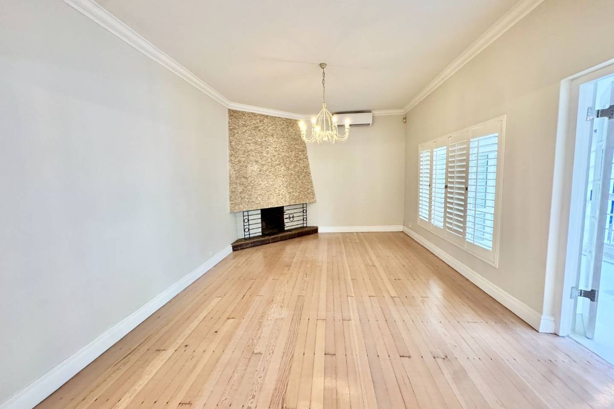 Spacious living room featuring polished timber flooring, a corner fireplace with stone cladding, crown molding, and white plantation shutters.
