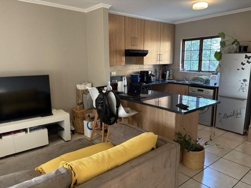 Open-plan living area featuring a functional kitchen with wood-finish cabinetry, granite countertops, and tiled flooring, seamlessly connected to the lounge space.