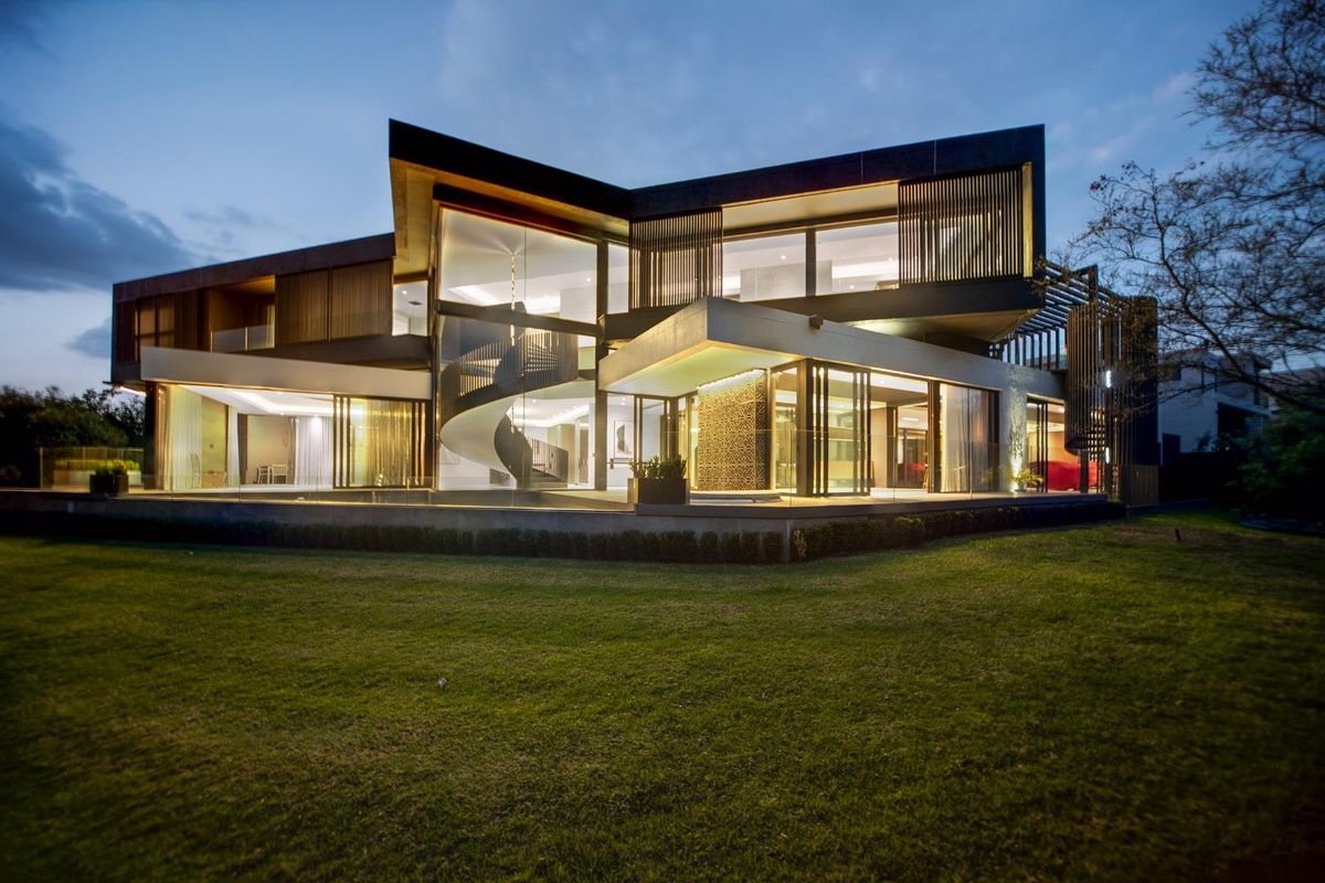 A striking modern architectural residence featuring expansive glass facades, a prominent spiral staircase, and integrated timber detailing overlooking a manicured rear garden.