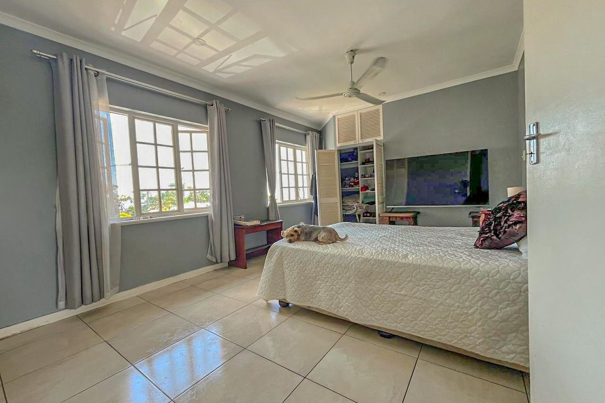 A spacious bedroom featuring tiled flooring, large windows with natural light, and a built-in cupboard with louvered doors.
