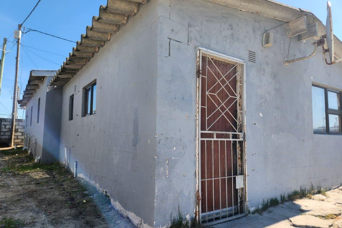 Exterior view of the rear building facade featuring a security gate, aluminium window frames, and a corrugated roof with visible signs of wear.
