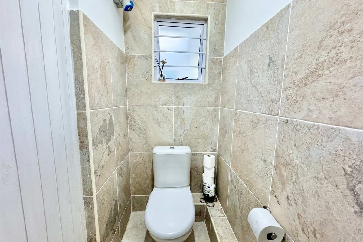 A compact bathroom featuring neutral floor-to-ceiling wall tiles, a modern toilet, and a small window with security bars.