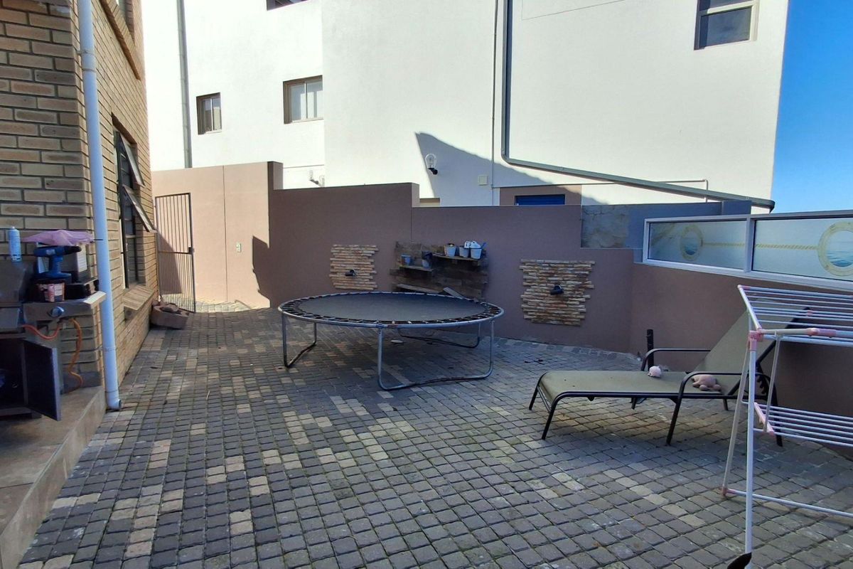 A paved rear courtyard area featuring boundary walls and a metal gate, providing a functional outdoor space.