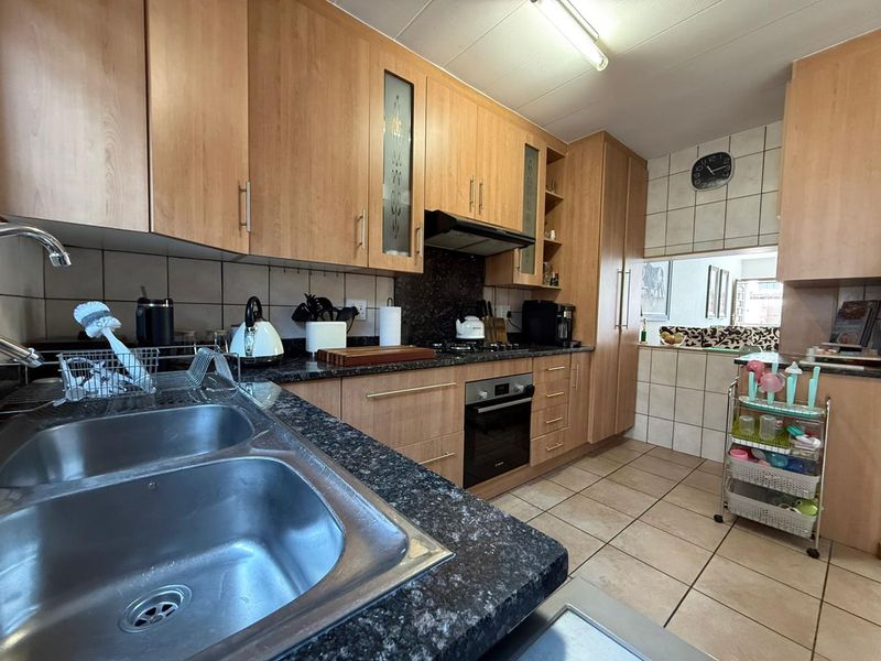 A functional kitchen featuring light wood cabinetry, granite countertops, a double basin sink, and built-in appliances including an oven and gas hob.