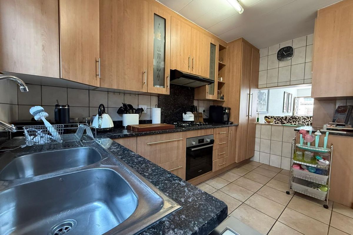 A functional kitchen featuring light wood cabinetry, granite countertops, a double basin sink, and built-in appliances including an oven and gas hob.
