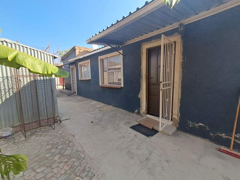 Rear exterior view of the property featuring a dark-painted facade, security gates, and concrete paving area.
