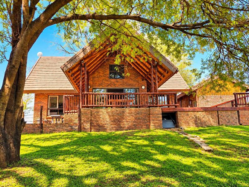 A charming brick-built structure featuring a prominent pitched roof, exposed timber beams, and a spacious wooden deck overlooking a well-maintained lawn.