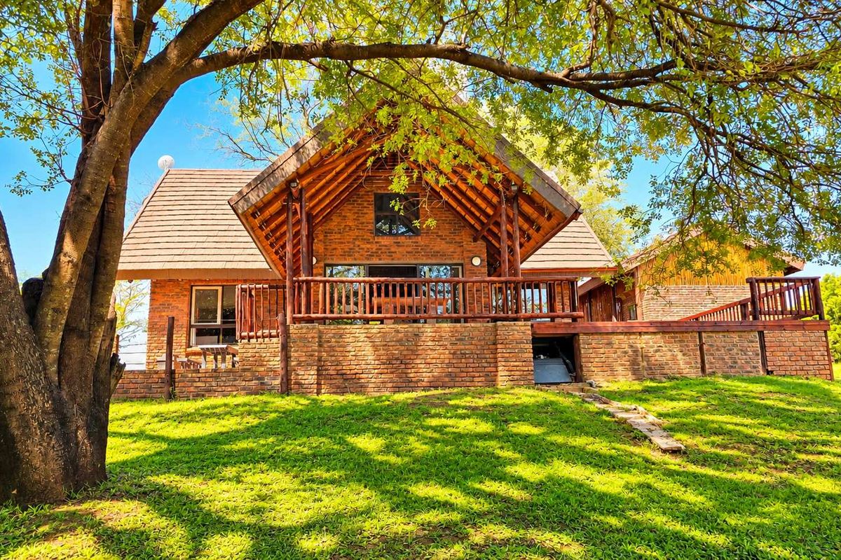 A charming brick-built structure featuring a prominent pitched roof, exposed timber beams, and a spacious wooden deck overlooking a well-maintained lawn.