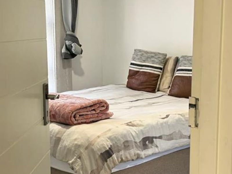 A compact bedroom featuring neutral tiled flooring and recessed ceiling lighting, viewed through a doorway.