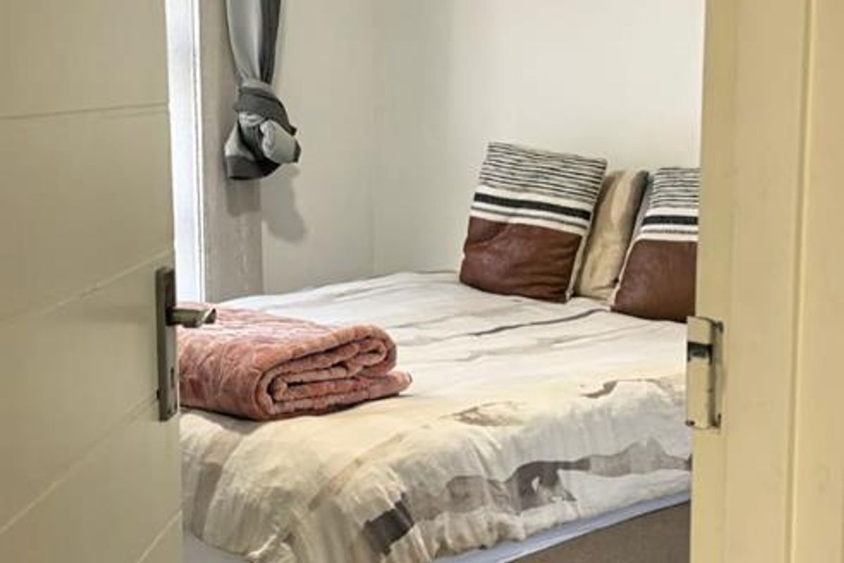 A compact bedroom featuring neutral tiled flooring and recessed ceiling lighting, viewed through a doorway.