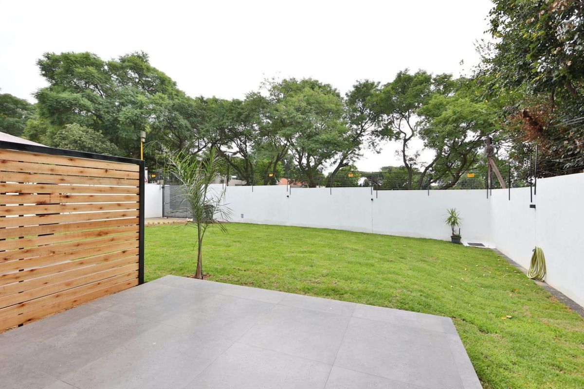 A well-maintained rear garden featuring a tiled patio, lush lawn, and secure perimeter wall with electric fencing and a modern timber privacy screen.